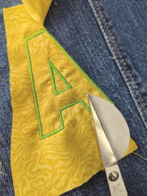 lettrine fablab. Aen tissu jaune appliqué sur du Jean. contour brodé à la machine.